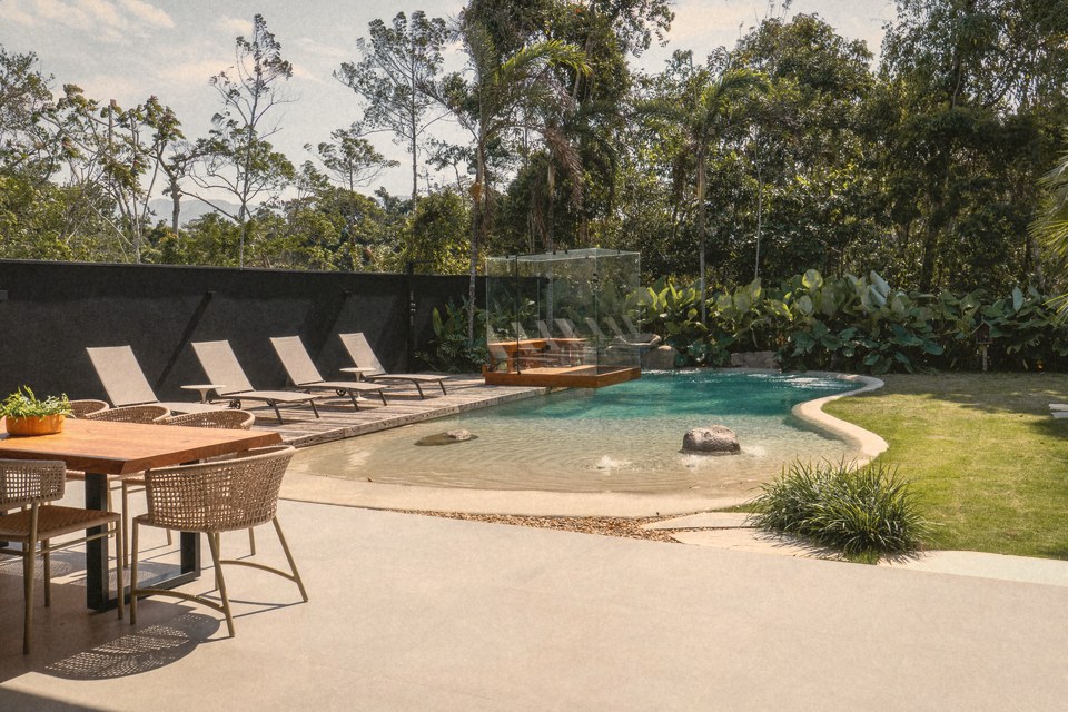 Uma piscina natural com praia de areia e espreguiçadeiras, num jardim