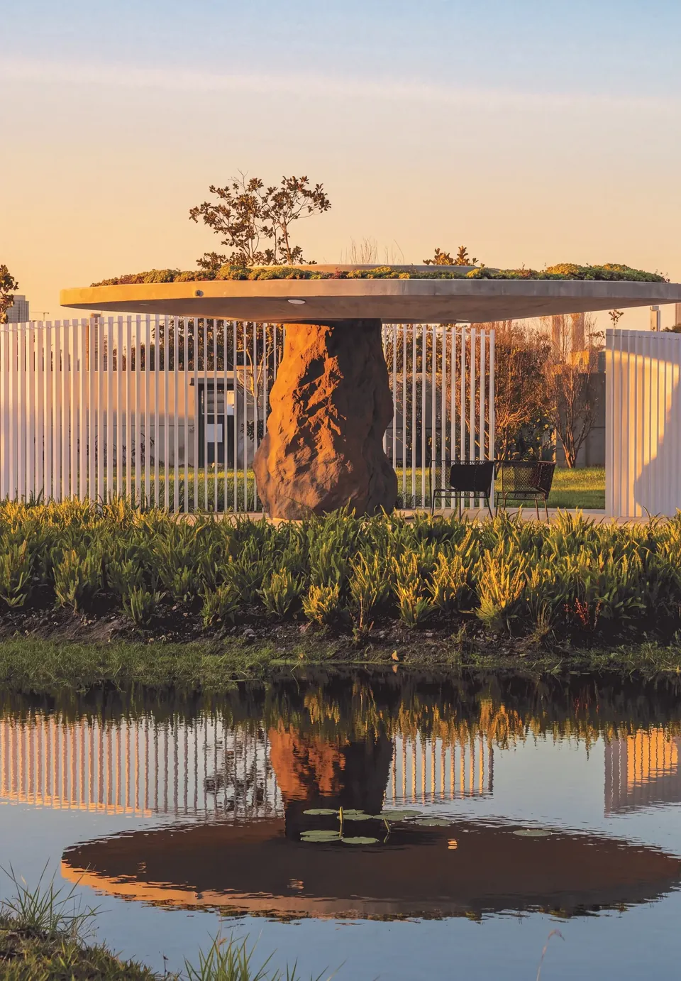 Pavilhão de Jader Almeida com a cobertura verde sobre um tronco de pedra, refletido na água
