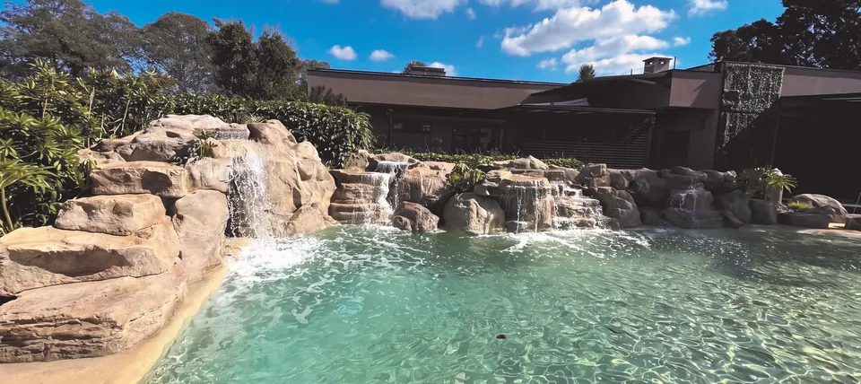 A cascata junto à casa: água, sombra e assento na mesma peça.