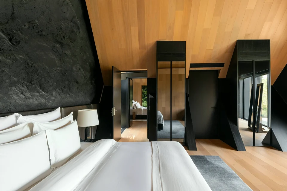 Suíte com parede de rocha escura ao lado da cama e piso de madeira